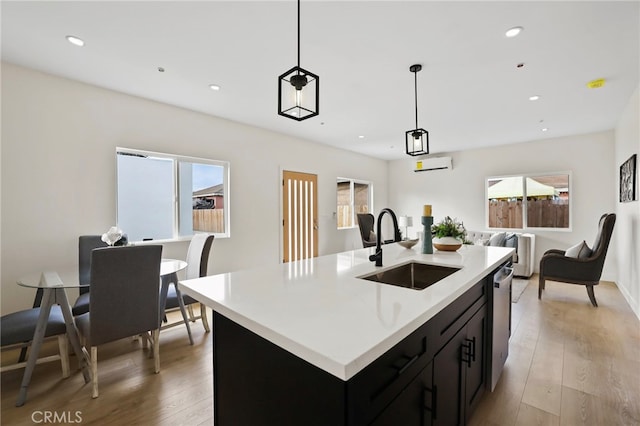 kitchen with dishwasher, light hardwood / wood-style flooring, decorative light fixtures, a center island with sink, and sink