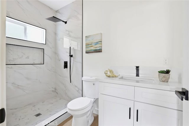 bathroom with tiled shower, vanity, and toilet