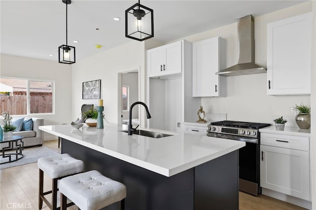 kitchen with white cabinetry, an island with sink, pendant lighting, stainless steel gas stove, and wall chimney range hood