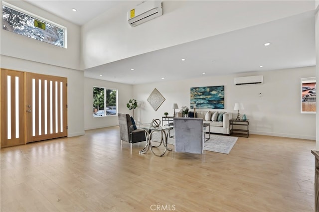 living room featuring light wood-type flooring, a wall unit AC, and a high ceiling