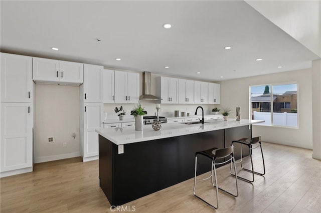 kitchen featuring a large island with sink, wall chimney exhaust hood, white cabinetry, and light hardwood / wood-style flooring