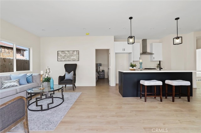 kitchen featuring light hardwood / wood-style flooring, wall chimney exhaust hood, hanging light fixtures, and white cabinetry