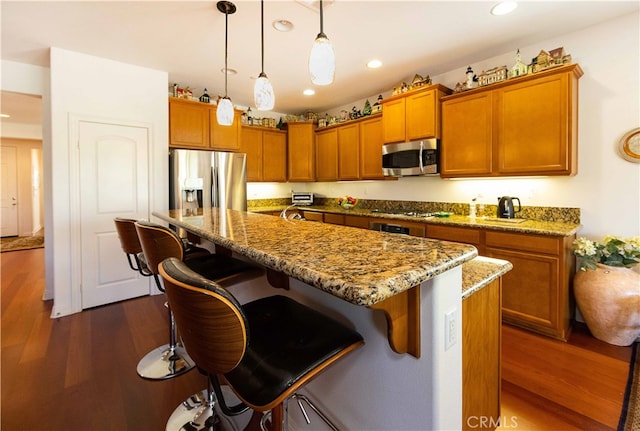 kitchen with appliances with stainless steel finishes, a kitchen island with sink, dark hardwood / wood-style floors, and a kitchen breakfast bar