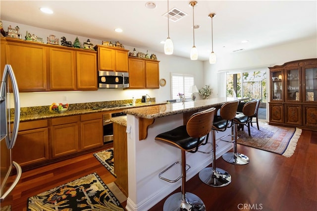 kitchen with decorative light fixtures, appliances with stainless steel finishes, dark hardwood / wood-style floors, and a kitchen bar