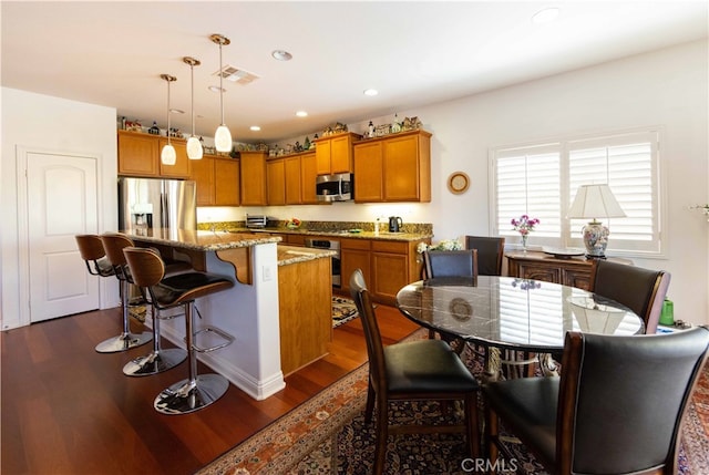 kitchen featuring appliances with stainless steel finishes, a kitchen island, a breakfast bar area, dark hardwood / wood-style flooring, and pendant lighting