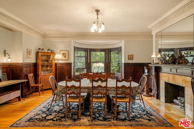 dining room with a notable chandelier, light wood-type flooring, crown molding, and a high end fireplace