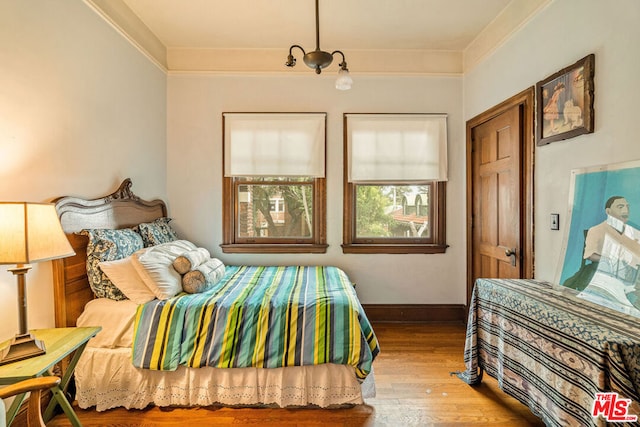 bedroom featuring a notable chandelier, wood-type flooring, and crown molding