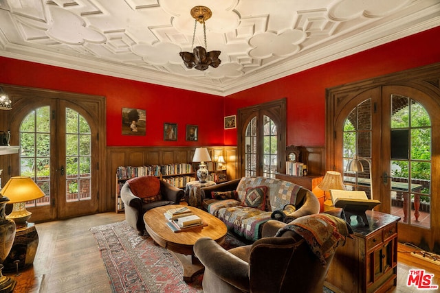 living room featuring a notable chandelier, light hardwood / wood-style floors, french doors, and crown molding