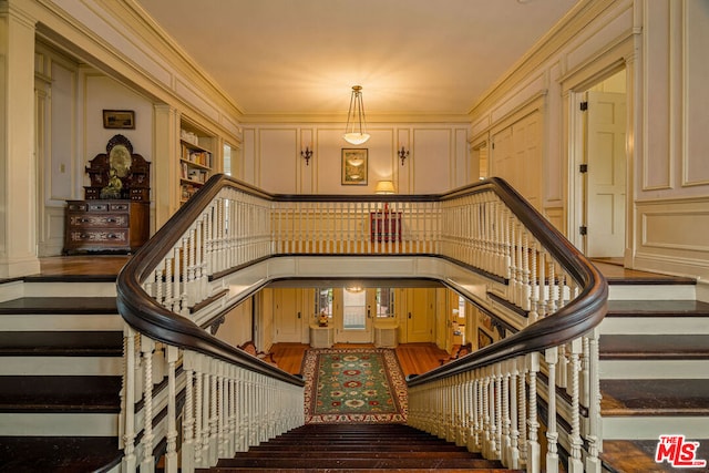 stairway with ornamental molding, built in shelves, and hardwood / wood-style floors