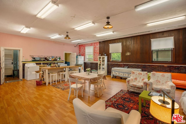 living room with brick wall, washer / clothes dryer, light wood-type flooring, and wood walls