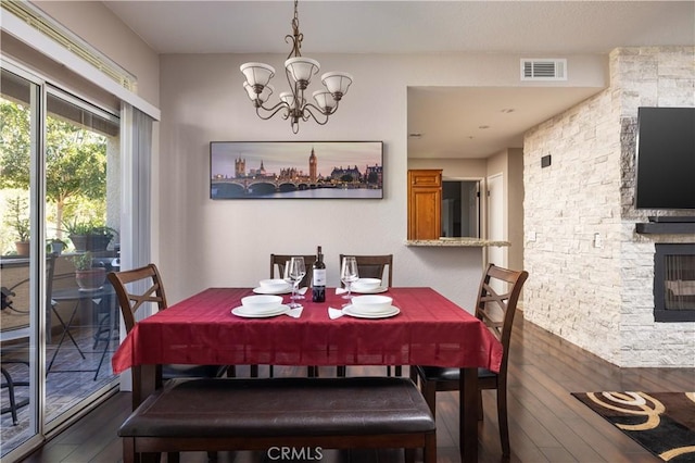 dining room with an inviting chandelier, dark hardwood / wood-style floors, and a stone fireplace