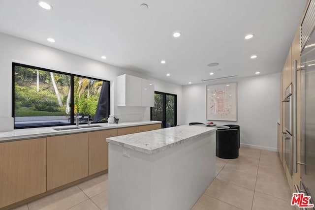 kitchen featuring white cabinets, a kitchen island, light tile patterned floors, light brown cabinetry, and sink