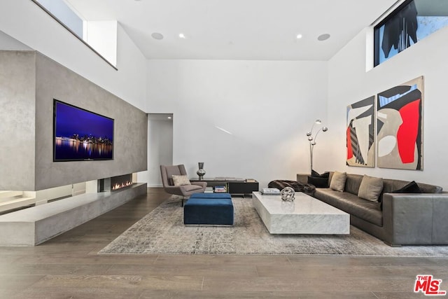 living room with hardwood / wood-style flooring, a multi sided fireplace, and a high ceiling