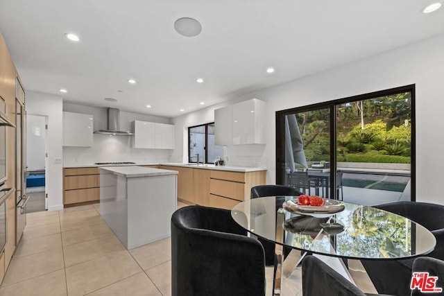 kitchen with white cabinetry, light tile patterned flooring, wall chimney exhaust hood, a kitchen island, and stovetop