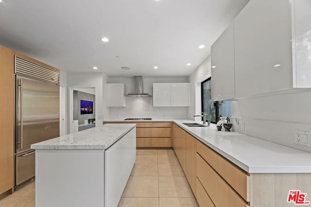 kitchen with stainless steel built in refrigerator, white cabinets, light tile patterned floors, wall chimney exhaust hood, and cooktop