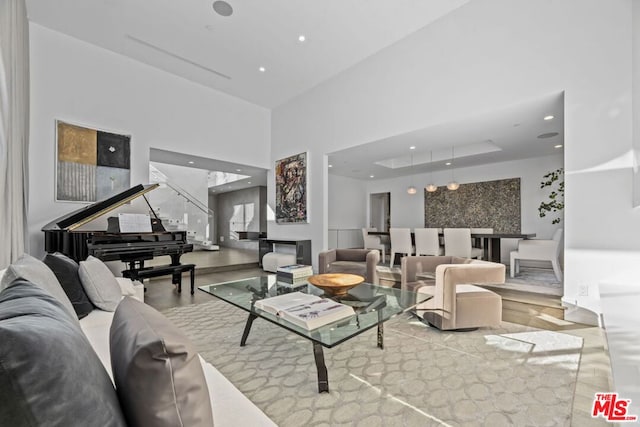 living room with light wood-type flooring, a raised ceiling, and a high ceiling