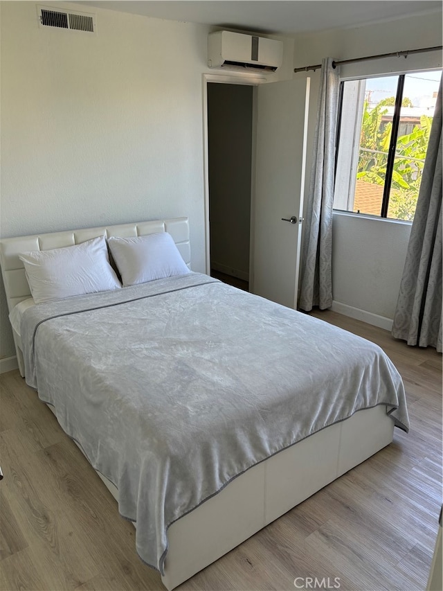 bedroom with light wood-type flooring and an AC wall unit