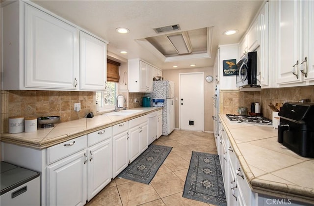 kitchen with white cabinets, tile counters, sink, and stainless steel appliances