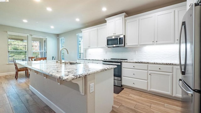 kitchen with white cabinetry, stainless steel appliances, a center island with sink, and sink