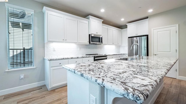 kitchen featuring a breakfast bar area, an island with sink, white cabinetry, appliances with stainless steel finishes, and light hardwood / wood-style floors