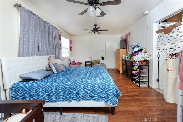 bedroom featuring ceiling fan, wooden walls, and dark hardwood / wood-style floors