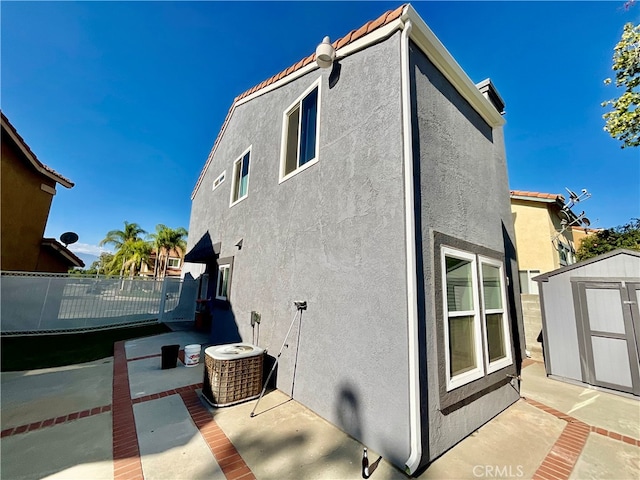 view of side of property featuring cooling unit, a storage unit, and a patio area