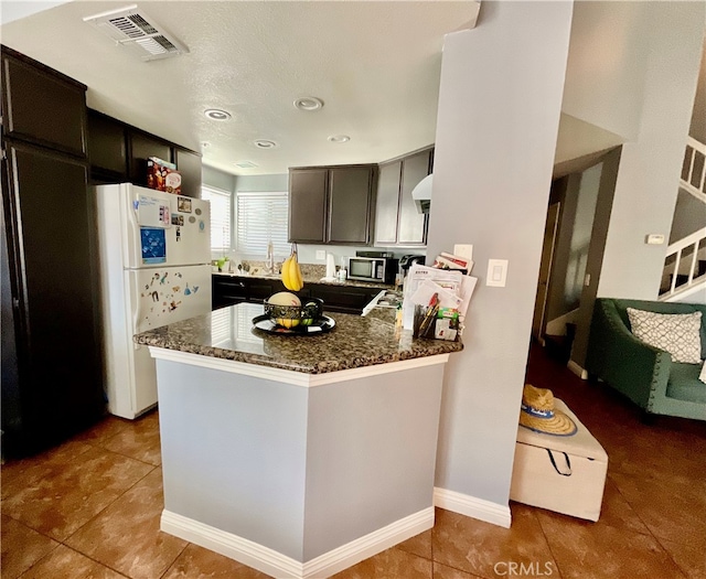 kitchen with kitchen peninsula, dark stone countertops, tile patterned flooring, and white refrigerator