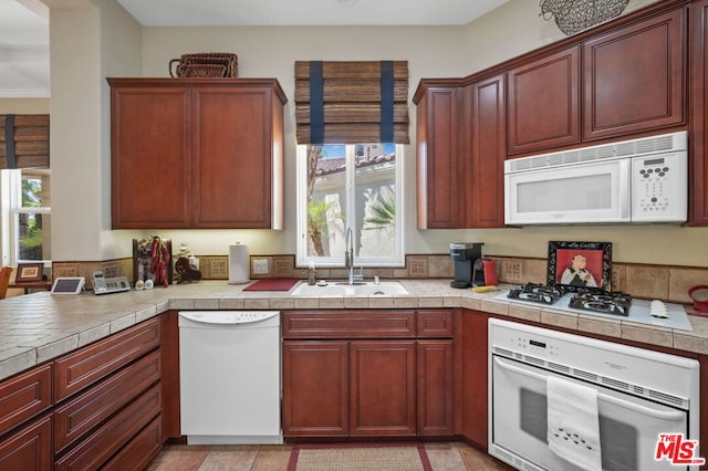 kitchen with white appliances, tile countertops, and sink