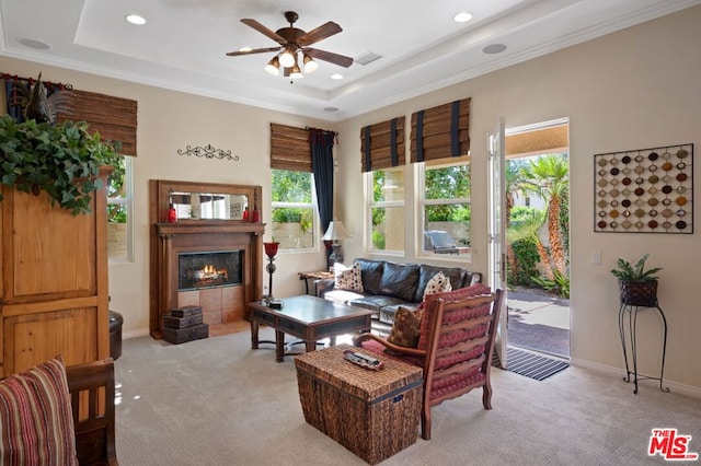 carpeted living room featuring a raised ceiling, ceiling fan, a tile fireplace, and a healthy amount of sunlight