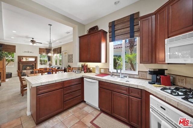 kitchen featuring sink, kitchen peninsula, hanging light fixtures, white appliances, and tile countertops