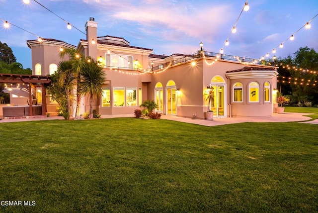 back house at dusk with a pergola, a patio area, and a lawn