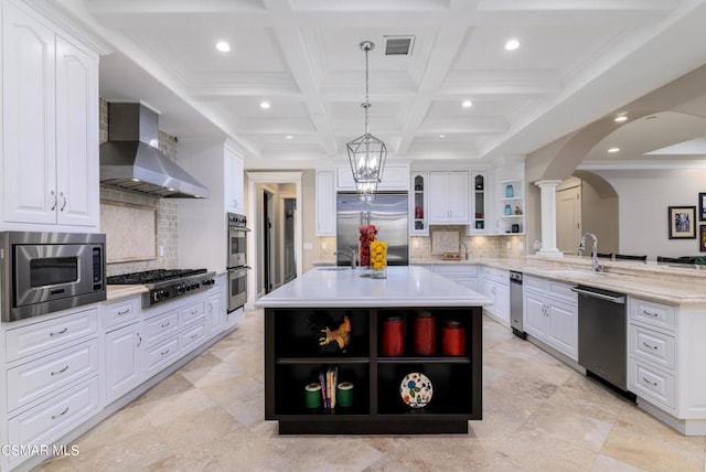 kitchen featuring backsplash, hanging light fixtures, a center island, built in appliances, and wall chimney exhaust hood