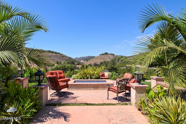 view of patio / terrace featuring an in ground hot tub, an outdoor fire pit, and a mountain view