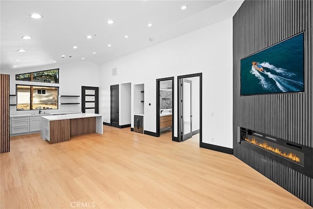 kitchen featuring light wood-type flooring, sink, high vaulted ceiling, a fireplace, and a kitchen island