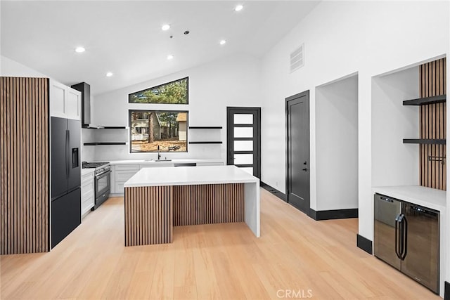 kitchen with a center island, high vaulted ceiling, wall chimney range hood, sink, and stainless steel gas range