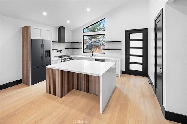 kitchen with a center island, stainless steel appliances, wall chimney exhaust hood, and light hardwood / wood-style floors