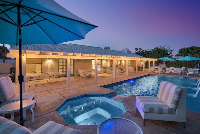 pool at dusk with an in ground hot tub, a patio area, and pool water feature