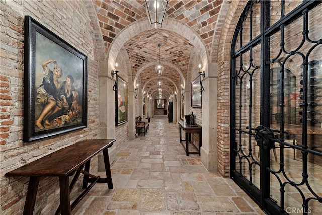 hall featuring lofted ceiling, brick ceiling, and brick wall