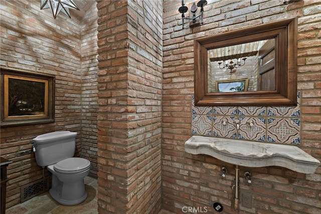 bathroom featuring toilet, brick wall, and backsplash