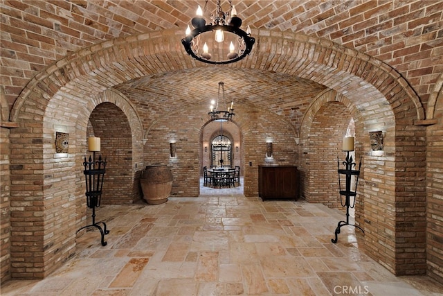 wine cellar with lofted ceiling, a notable chandelier, brick ceiling, and brick wall