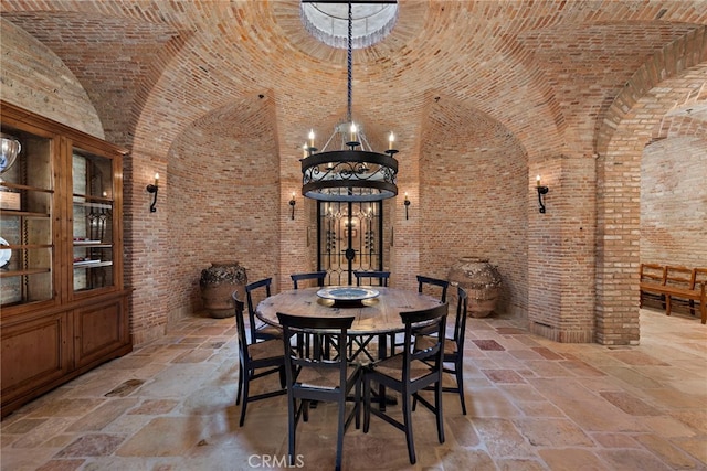 unfurnished dining area featuring a towering ceiling, brick ceiling, a notable chandelier, and brick wall