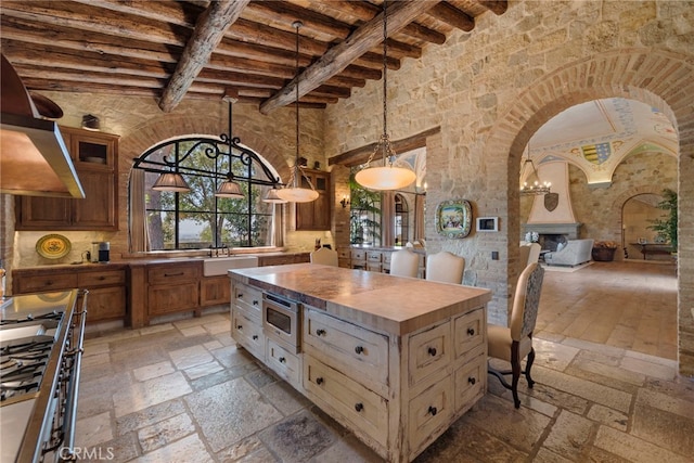 kitchen with pendant lighting, beamed ceiling, appliances with stainless steel finishes, range hood, and butcher block counters