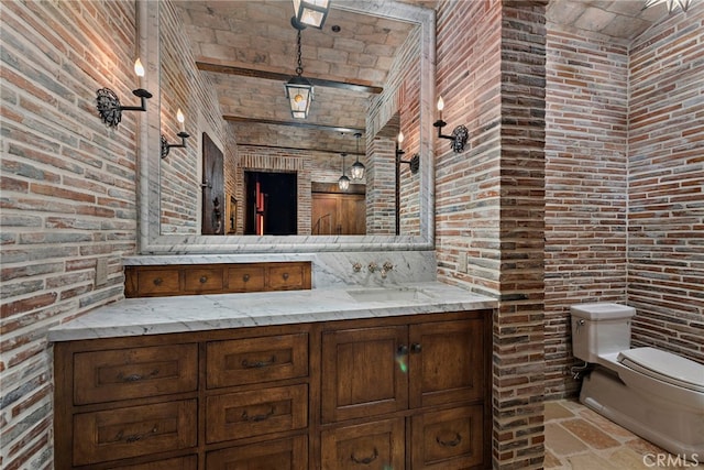 bathroom featuring brick wall, brick ceiling, vanity, and toilet