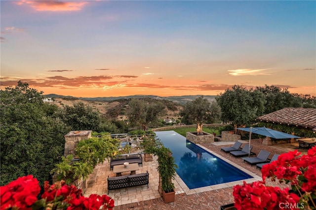 pool at dusk featuring a mountain view and a patio