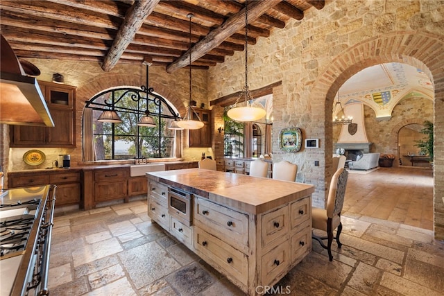 kitchen with wall chimney exhaust hood, wooden counters, a high ceiling, appliances with stainless steel finishes, and beam ceiling