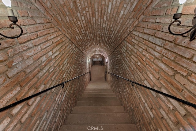 staircase with lofted ceiling and brick wall