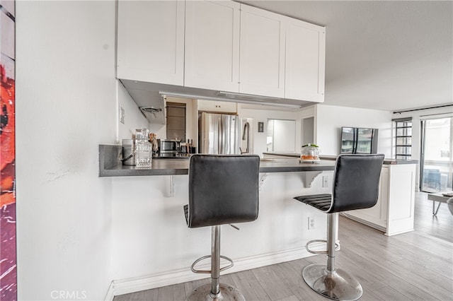 kitchen featuring stainless steel refrigerator, a kitchen breakfast bar, kitchen peninsula, and white cabinetry