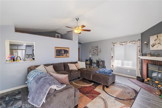 living room featuring lofted ceiling, hardwood / wood-style floors, ceiling fan, and a brick fireplace