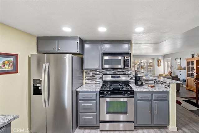 kitchen with a textured ceiling, backsplash, gray cabinets, appliances with stainless steel finishes, and light wood-type flooring