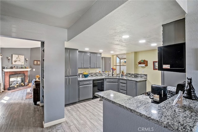 kitchen with kitchen peninsula, gray cabinetry, a brick fireplace, dishwasher, and light wood-type flooring